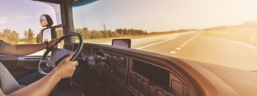 truck driver gripping steering wheel inside cab on open highway