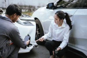 insurance agent with clipboard inspecting vehicle damage with woman pointing at bumper